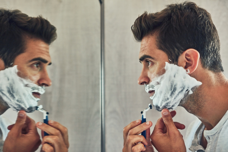 Мужчина бреется перед зеркалом.