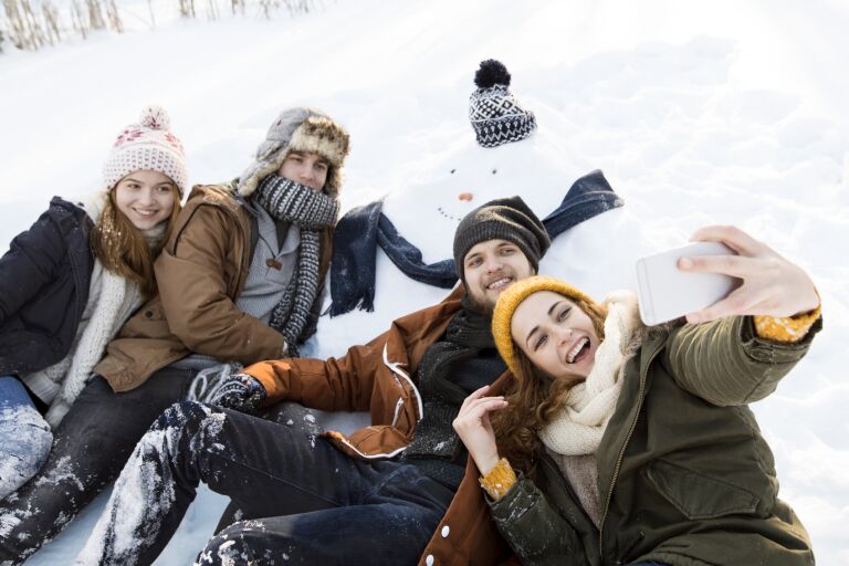 молодые люди в зимней одежде делают селфи со снеговиком в зимнем пейзаже