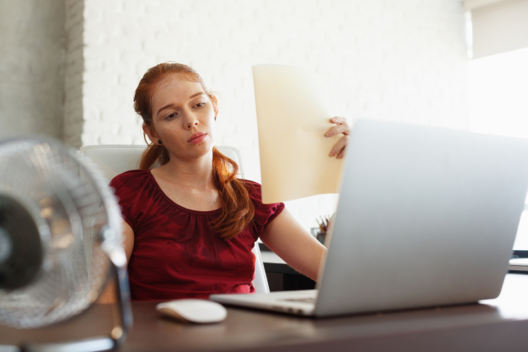 усталая девушка в красной майке сидит за компьютером, стресс приводит к проблемам кожи