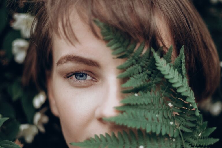 Женское лицо, наполовину спрятанное за зелеными листьями папоротника