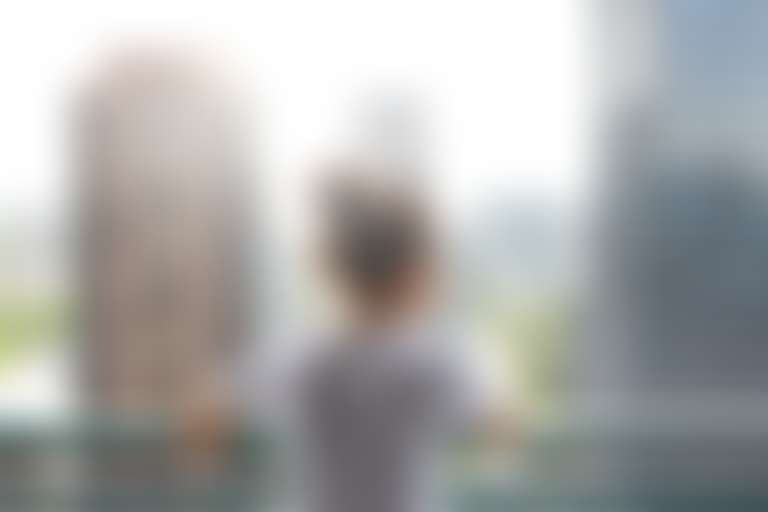 темноволосая девушка с собранными в пучок волосами стоит на балконе высокого этажа с видом на большой город