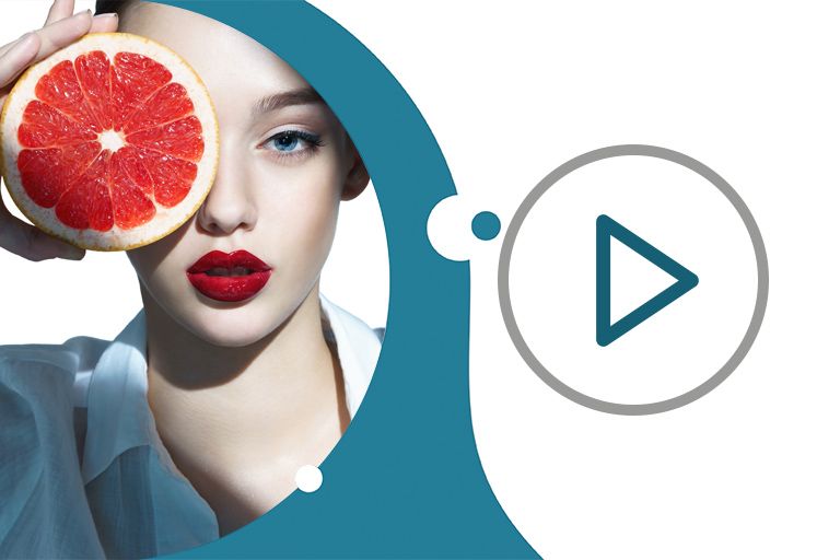 голубоглазая девушка с ухоженной кожей и накрашенными ярко-красной помадой губами прикладывает к глазу аппетитный большой круг грейпфрута
