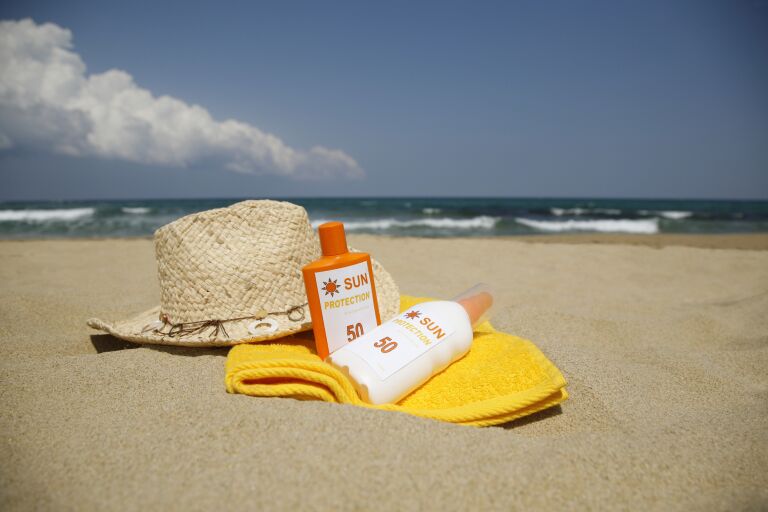 Композиция на пляже: солнцезащитные кремы на желтом полотенце, соломенная шляпа