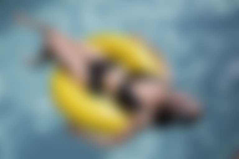 девушка в черном купальнике и солнцезащитных очках загорает на воде в желтом круге.
