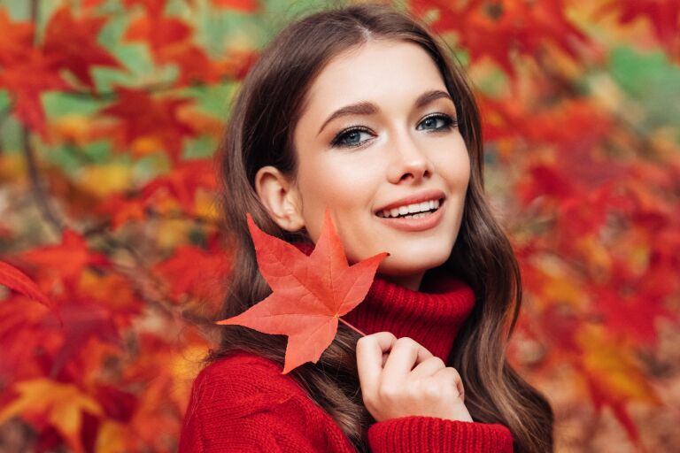 девушка с роскошными волосами в красном свитере на фоне осенних красных листьев