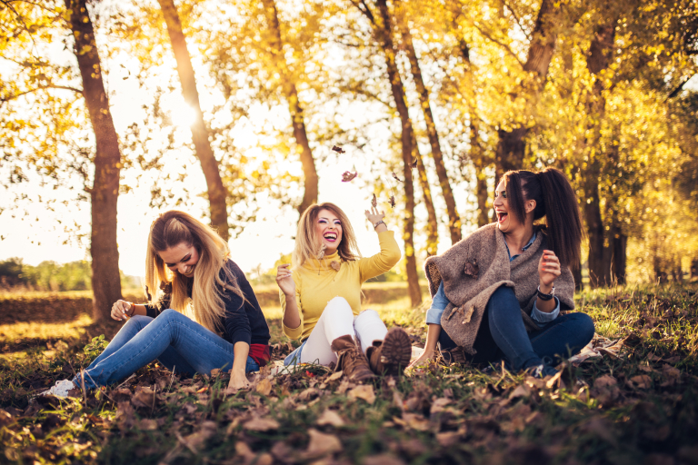 Три веселые девушки сидят на земле в осеннем лесу