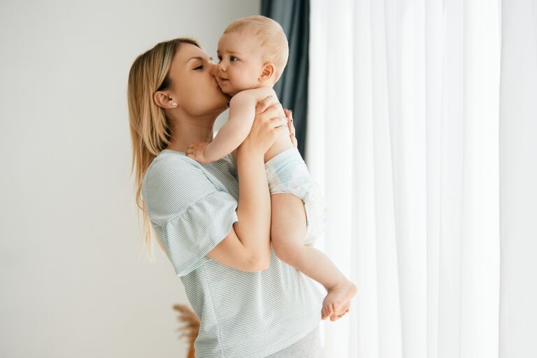 ухоженная стройная молодая мама держит на руках и целует малыша