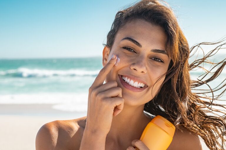 девушка с загорелой кожей на берегу моря наносит на лицо солнцезащитный крем