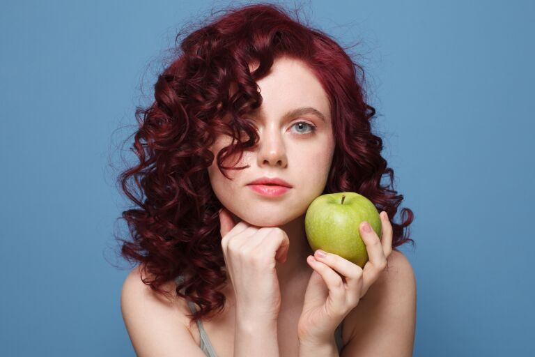 девушка с пышными кудрявыми волосами держит зеленое яблоко