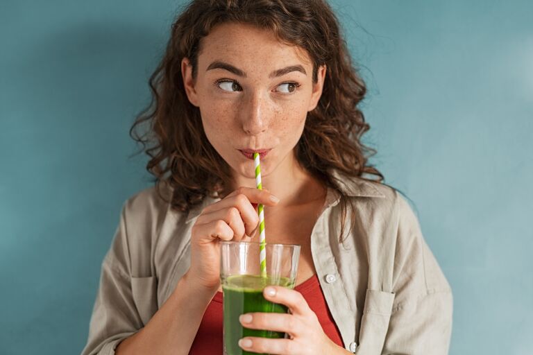 Девушка пьет смузи из низкокалорийный овощей и зелени – все для похудения.