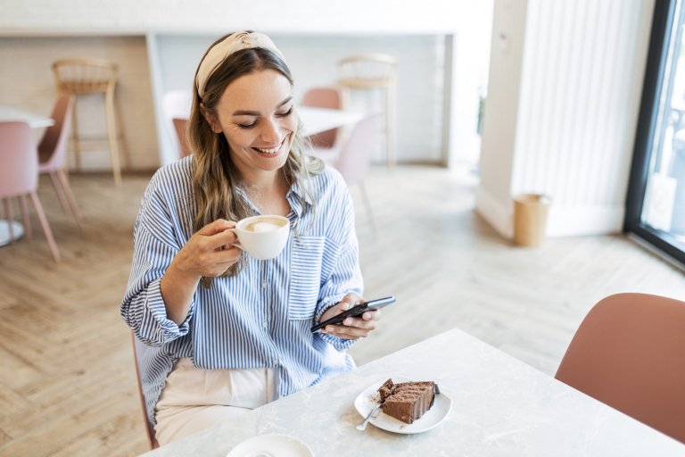 девушка с ухожоенной кожей пьет кофе и ест маленький кусочек торта