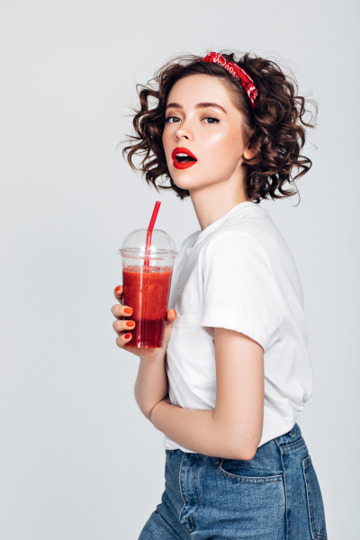Девушка с красной помадой держит в руках стакан с красным напитком и соломинкой
