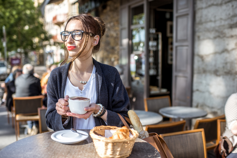 Девушка пьет кофе в кофейне на улице.