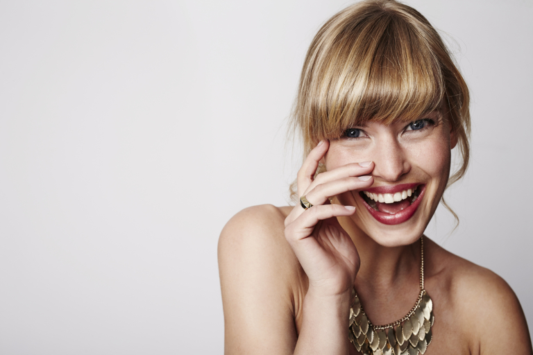 Девушка улыбается и держит руку у глаз.