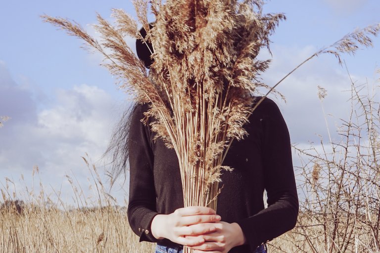 Девушка в темном с букетом колосков - символ сухих волос - на фоне поля с соломой