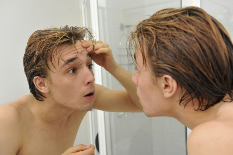 Молодой человек рассматривает своё лицо в зеркале