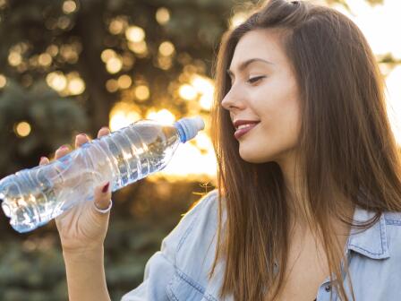 Девушка в парке держит в руке перед собой бутылку воды